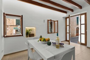 A dining area with a table, chairs, a bowl of fruit, and a bottle. There are windows and a view of an outdoor area. - Can Mayol, beautiful, newly refurbished village house at few steps from centre. (Fornalutx)