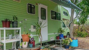 Een groene camper met een veranda, plantenbakken, een tafeltje en een stoel.
