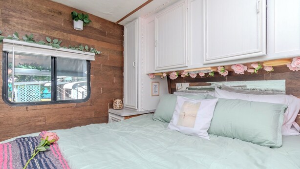 Een slaapkamer met een bed, een raam, houten wanden en een witte kast.