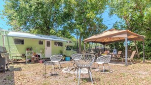 Een groene camper met een overdekte patio, buiten zitplaatsen en een vuurkorf.