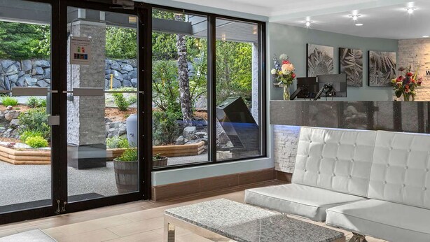 A reception area with a stone wall, a white cushioned bench, and a reception desk. - Christmas in Whistler!   1 bedroom + den condo. Walk to the slopes!  (Whistler)