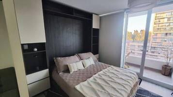A modern bedroom with a bed, built-in wardrobe, and a large window with a view of buildings.