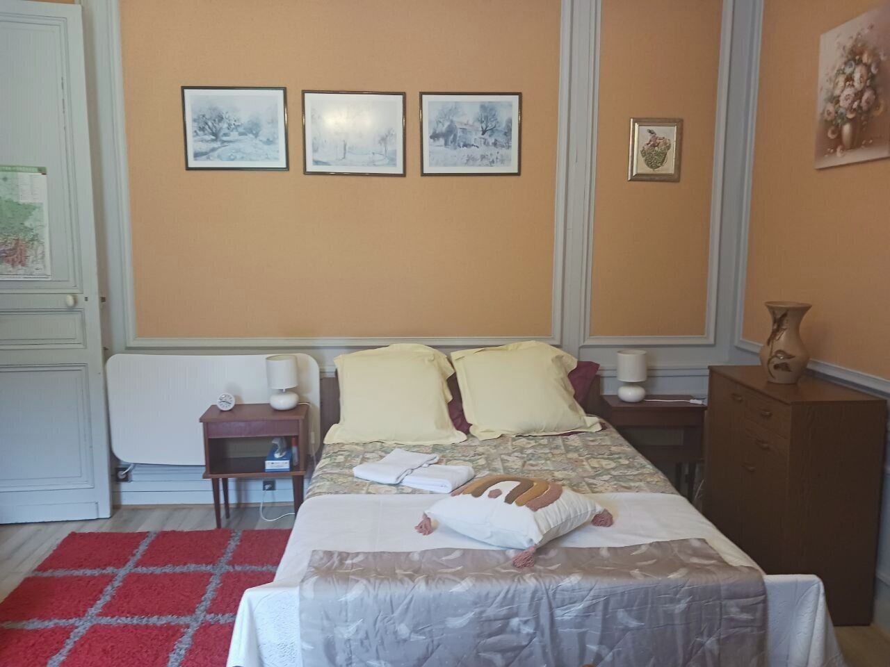 A bedroom with a bed, bedside tables, a radiator, and wall-mounted pictures.