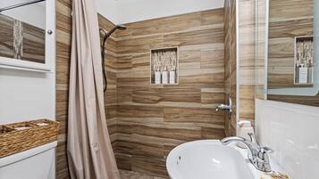 A bathroom with a shower, a sink, a mirror, and a toilet.