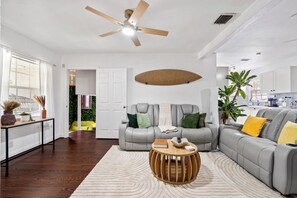 A modern living room with a sofa, a round wooden coffee table, and a ceiling fan. - Palm Paradise Resort! Beach Area, Pool, Sauna, Cold Plunge, Hot Tub - Zen Zone (Lake Worth Beach)