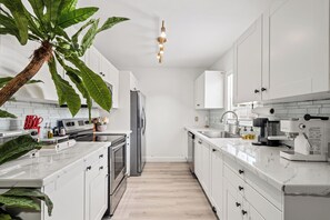 A modern kitchen with white cabinets, a marble countertop, a refrigerator, an oven, and a coffee machine. - Palm Paradise Resort! Beach Area, Pool, Sauna, Cold Plunge, Hot Tub - Zen Zone (Lake Worth Beach)