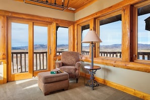 A cozy room with a large window, a chair, a small table, and a book on the ottoman.