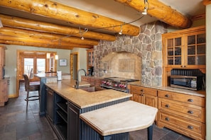 A kitchen with a stone fireplace, wooden beams, and a granite countertop.