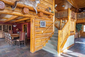 A log cabin interior with a wooden staircase, a dining area with a table and chairs, and a mounted animal head on the wall. - Mountain Wedding & Retreat Destination with Private Lodge, 55 acres, Sleep 37 (Granby)