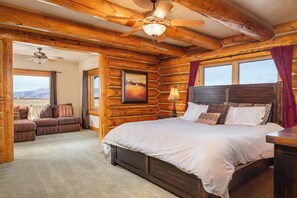 A log cabin bedroom with a large bed, a sofa, and a ceiling fan. - Mountain Wedding & Retreat Destination with Private Lodge, 55 acres, Sleep 37 (Granby)