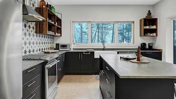 Une cuisine moderne dotée d’un grand îlot central, d’appareils électroménagers intégrés et offrant une vue sur les arbres par la fenêtre.