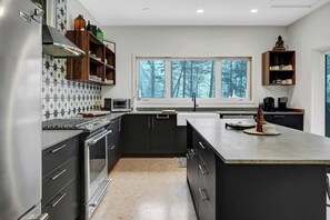 A modern kitchen with a large island, built-in appliances, and a view of trees through the window.