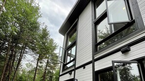 A modern two-story building with large windows, a wooden deck, and a forested background.