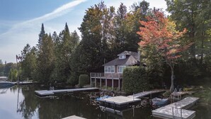 A house with a dock extending into a calm lake, surrounded by trees and a clear sky.