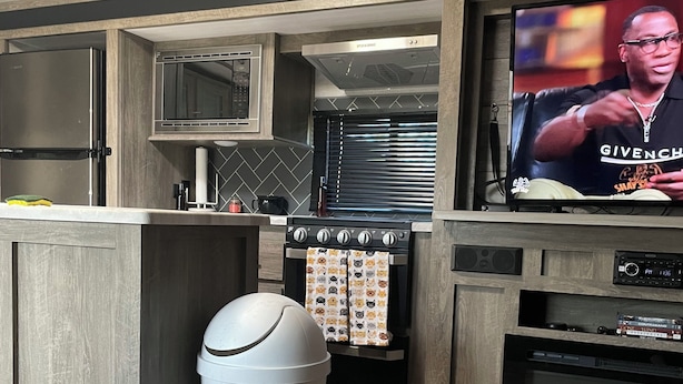 A modern kitchen with a built-in microwave, oven, and a television displaying a man.