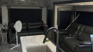 A modern kitchen with a built-in sink, a fan, and a black leather sofa.