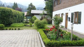 Un patio con un sendero empedrado, un edificio de madera y un jardín con flores rojas y blancas.