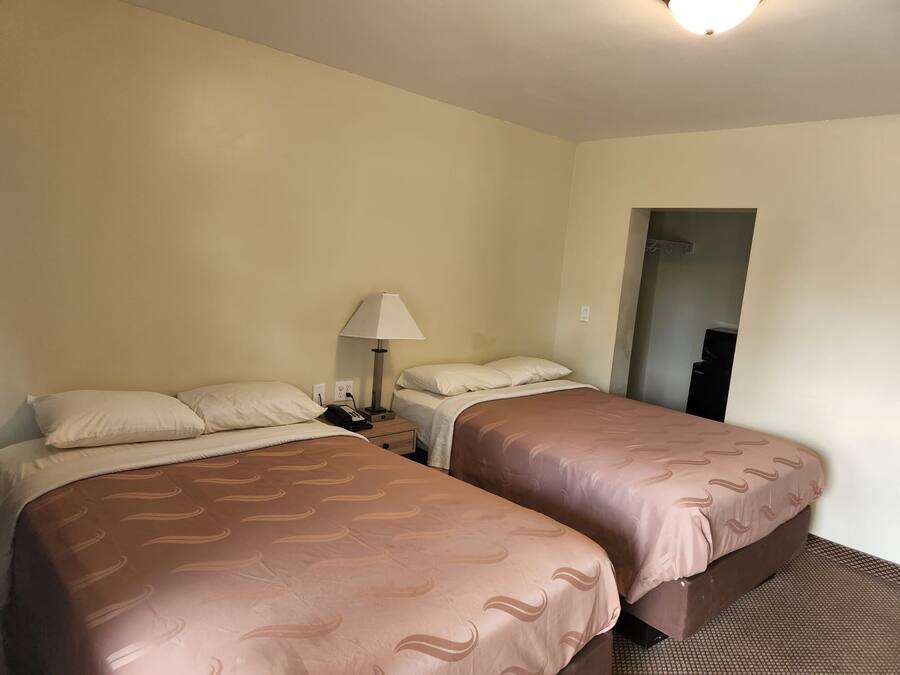 Una camera d'albergo con due letti, un comodino con una lampada e un armadio.