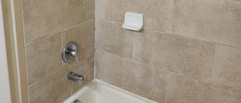 A bathroom with a bathtub, a shower, and a hand soap dispenser on the wall.
