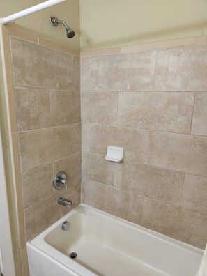 Un baño con bañera, ducha y dispensador de jabón en la pared.