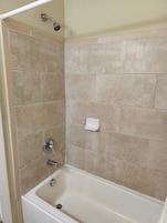A bathroom with a bathtub, a shower, and a hand soap dispenser on the wall.