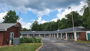 A motel with a row of rooms, a parking lot, and a grassy area with a utility building.