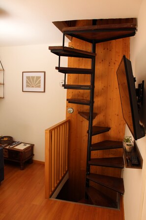 A spiral staircase with a wooden finish, a small table with a plant, and a framed picture on the wall. - The Spiral House (Liguria)