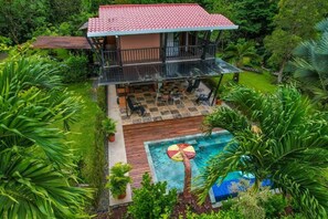 Una casa de dos pisos con balcón, piscina y abundante vegetación.