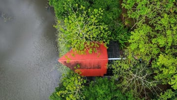 A red-roofed building surrounded by dense green foliage, adjacent to a body of water.