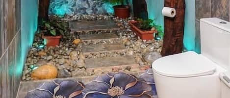 A bathroom with a stone wall, a white toilet, and a small sink.