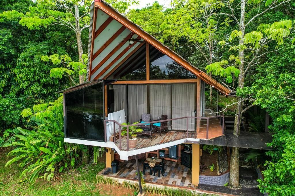 Una casa moderna con balcón de vidrio, rodeada de abundante vegetación.