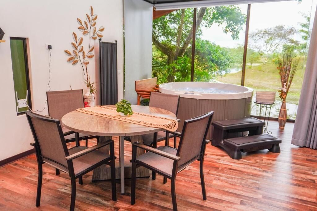 A modern dining area with a round table, chairs, a hot tub, and a view of greenery.