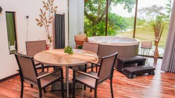 A modern dining area with a round table, chairs, a hot tub, and a view of greenery.