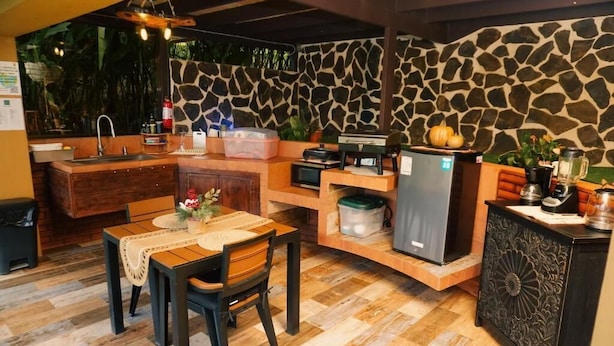 Uma cozinha compacta com parede de pedra, armários de madeira, uma mesa de jantar com cadeiras e uma geladeira.