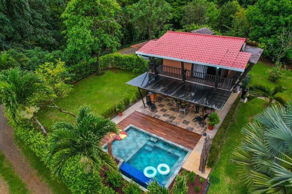 Una casa de dos plantas con techo de tejas rojas, piscina y patio.