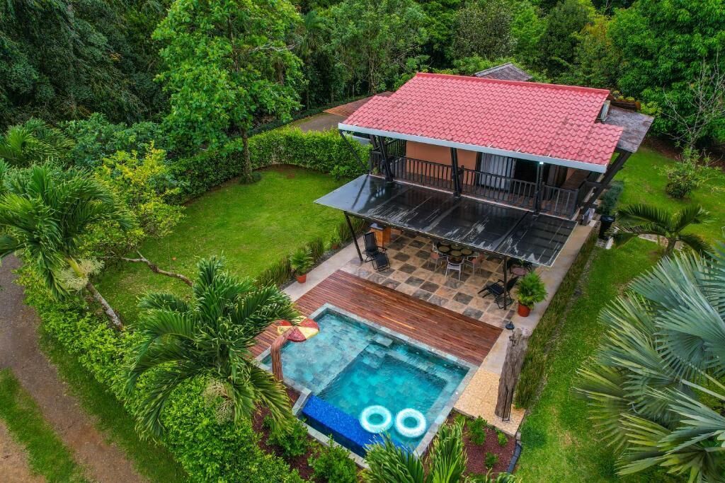 A two-story house with a red roof, a swimming pool, and a patio area.
