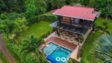 A two-story house with a red roof, a swimming pool, and a patio area.