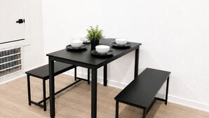 A dining area with a black table and benches, white walls, and a painting of wine bottles above the table.