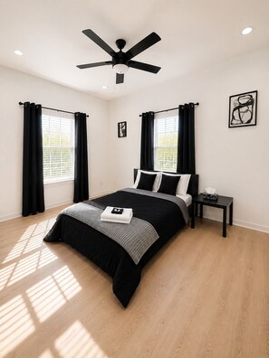 A bedroom with a bed, a nightstand, a ceiling fan, and a window with curtains.