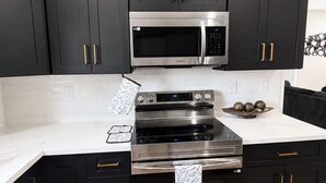 A kitchen with black cabinets, stainless steel appliances, and a white countertop.