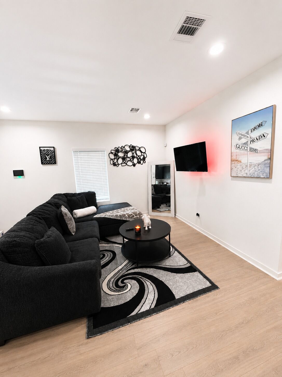 En moderne stue med en sort sofa, et rundt sofabord og et vægmonteret tv.
