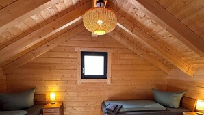 Et hyggeligt soveværelse på loftet med skråvægge, to senge, et lille vindue og en hængende lampe.