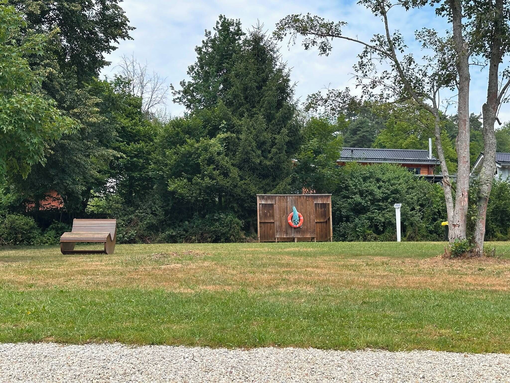 A wooden bench, a small shed, and a grassy area with trees in the background.