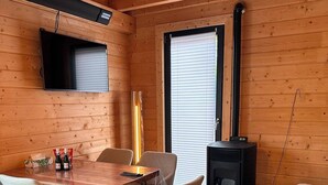 Et træinteriør med et spisebord, stole, et TV ophængt på væggen og en brændeovn.