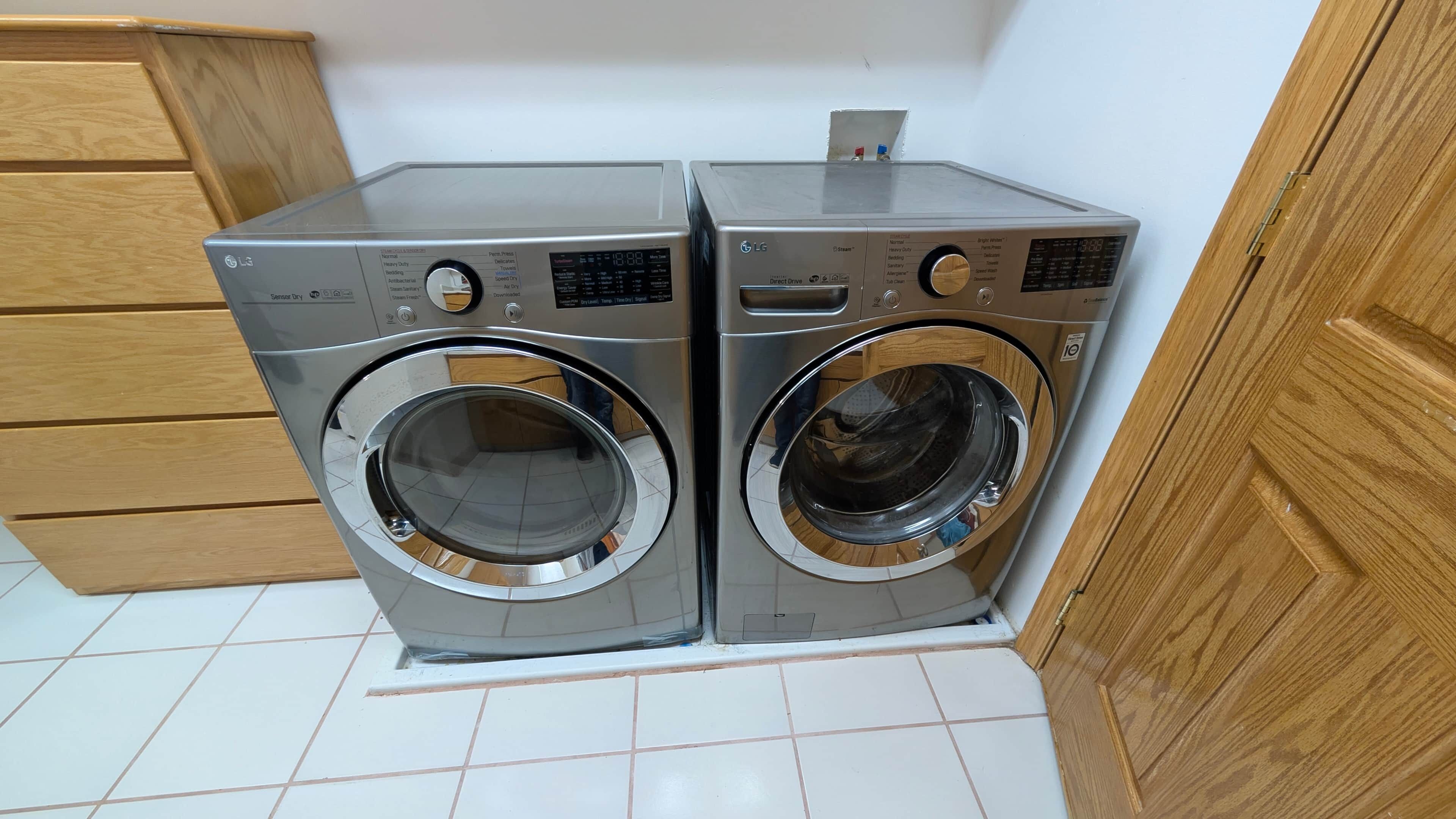 Deux lave-linge à chargement frontal de la marque LG, installés dans une buanderie avec des armoires en bois et un revêtement de sol en carrelage blanc.