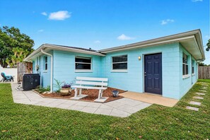 A light blue house with a dark blue door, a white bench, and a small garden area. - Family and dog friendly home with private pool (Largo)