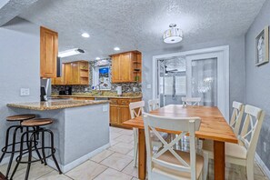 A kitchen with wooden cabinets, a granite countertop, and a dining area with a wooden table and white chairs. - Family and dog friendly home with private pool (Largo)