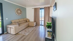 A living room with a sectional sofa, a flat-screen TV, a decorative wall piece, and a large window with curtains.