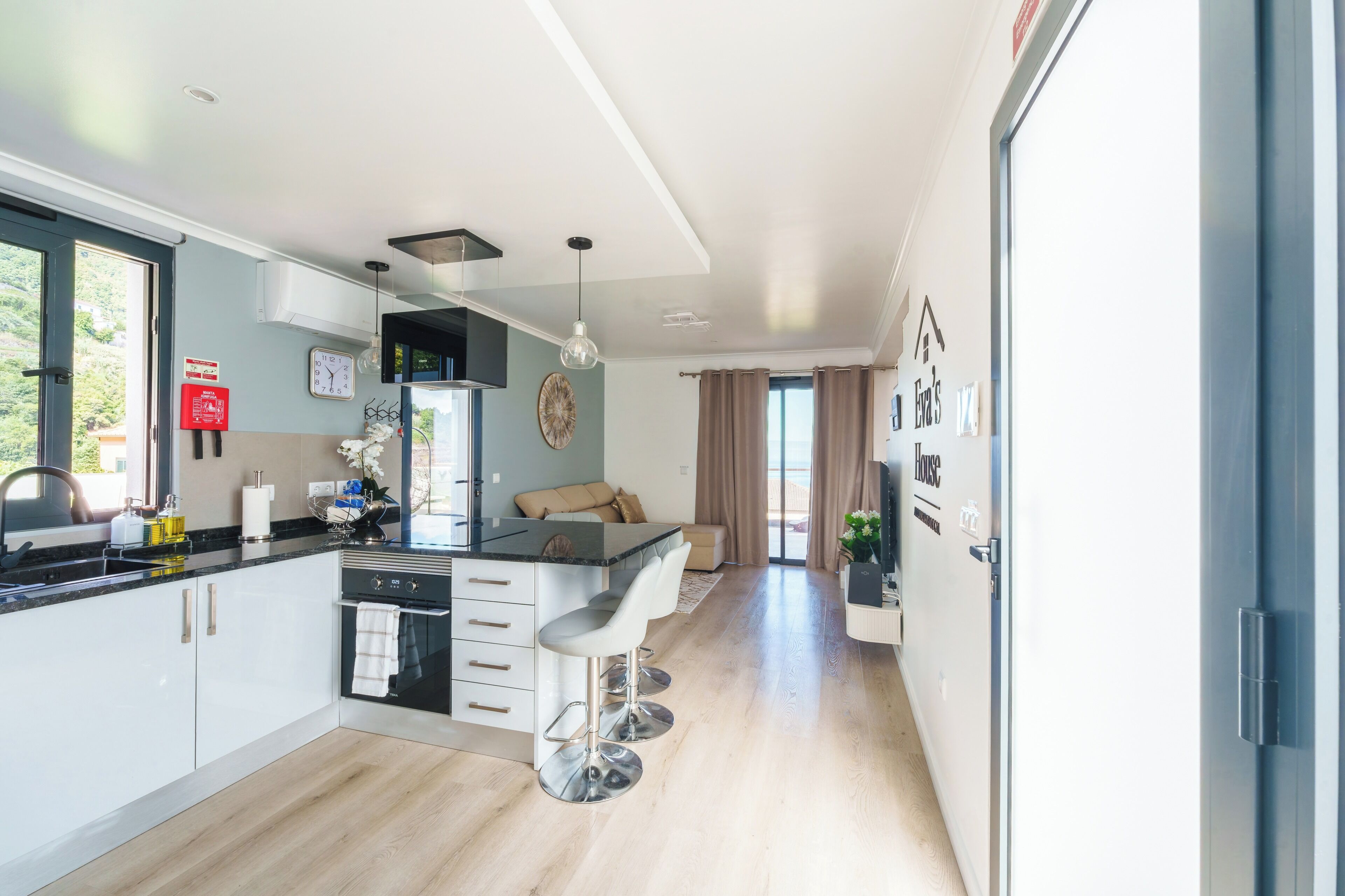 A modern kitchen with a central island, a dining area with a sofa, and a view of the outdoors.