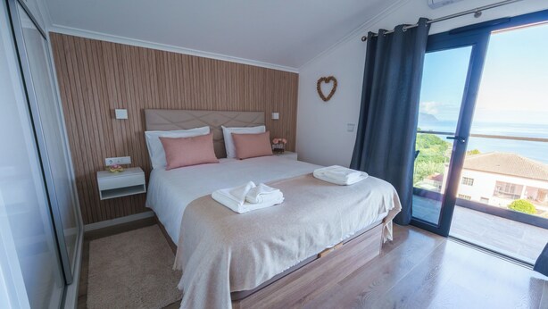 A hotel room with a bed, bedside tables, a view of the sea, and a heart-shaped decoration on the wall.